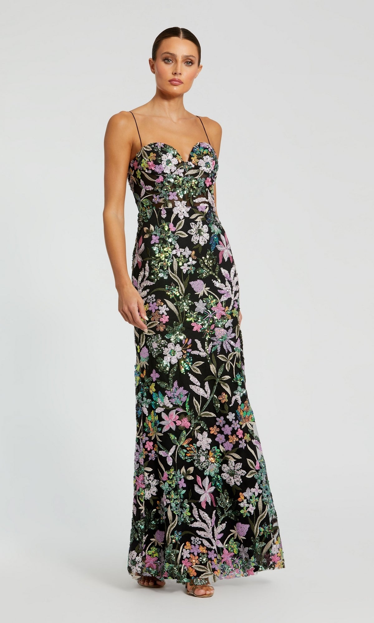 A woman wears the Sequin-Print Black Formal Dress: Mac Duggal 49827, a black evening gown with thin straps and colorful floral embroidery, set against a plain light background.